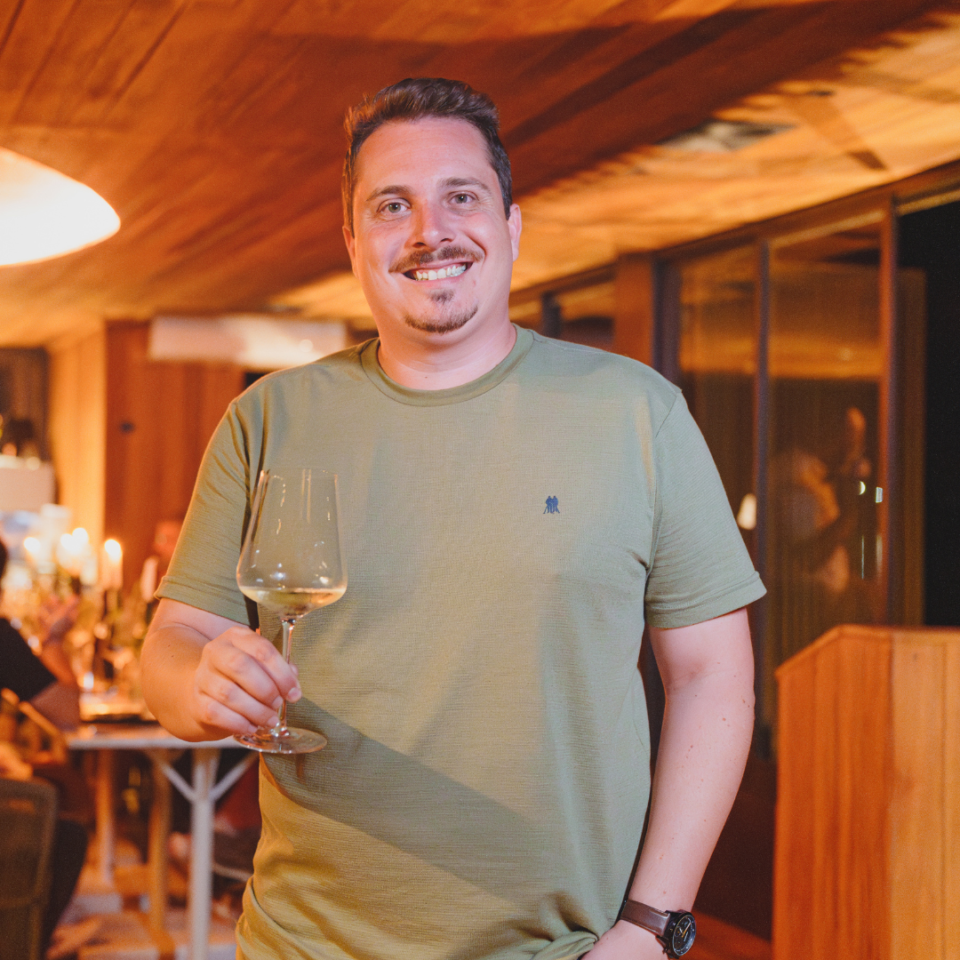 Um homem com barba está vestindo uma camisa branca e sorrindo.