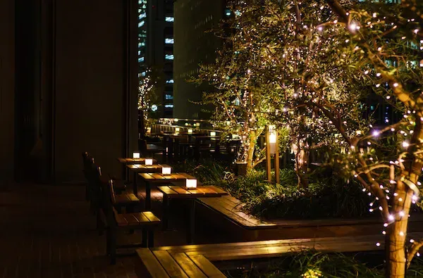 A row of tables and benches are lit up at night.