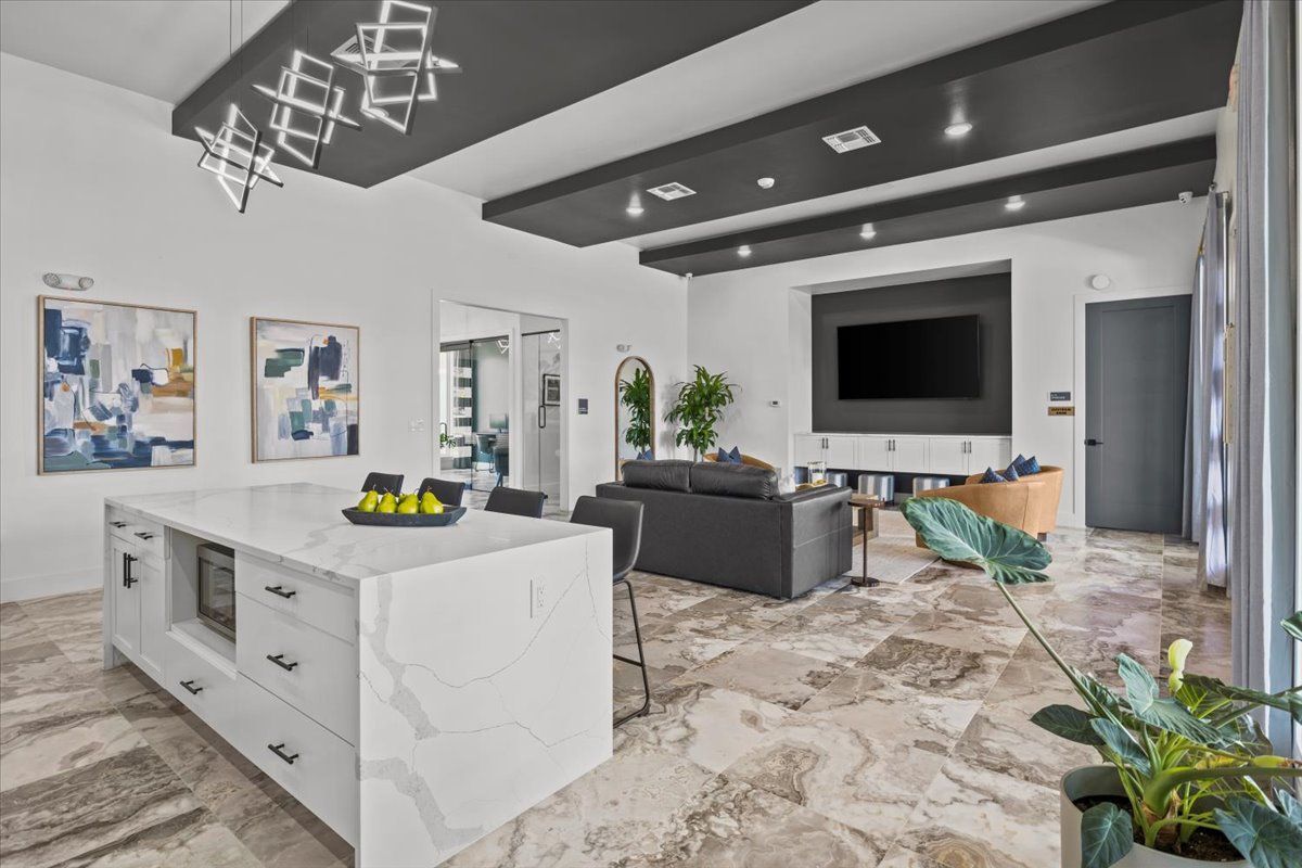 Modern open-plan living space with kitchen island, living room with TV, gray sofa, and decorative stone floor.