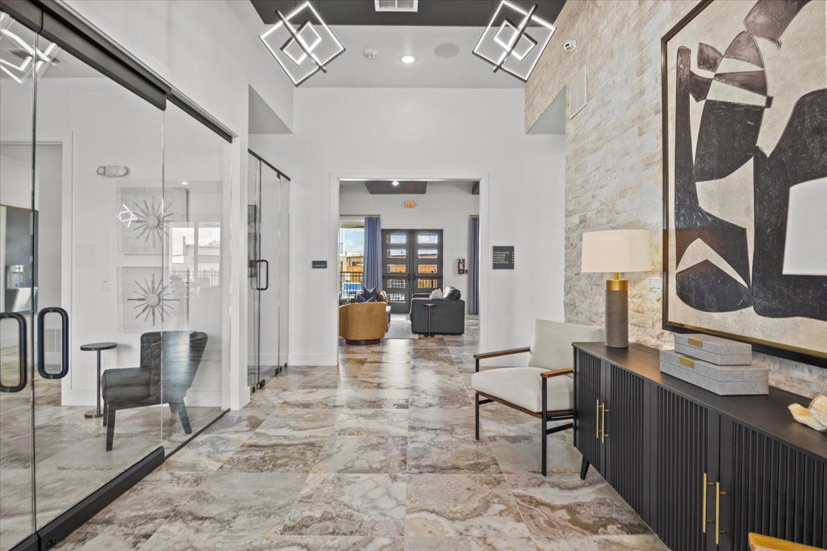 Modern entryway with glass doors, stone flooring, and artwork. Features a black console and chairs.