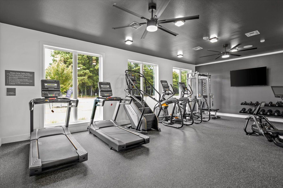 Gym with treadmills, elliptical machines, and weights. Features windows, dark ceiling, and rubber flooring.