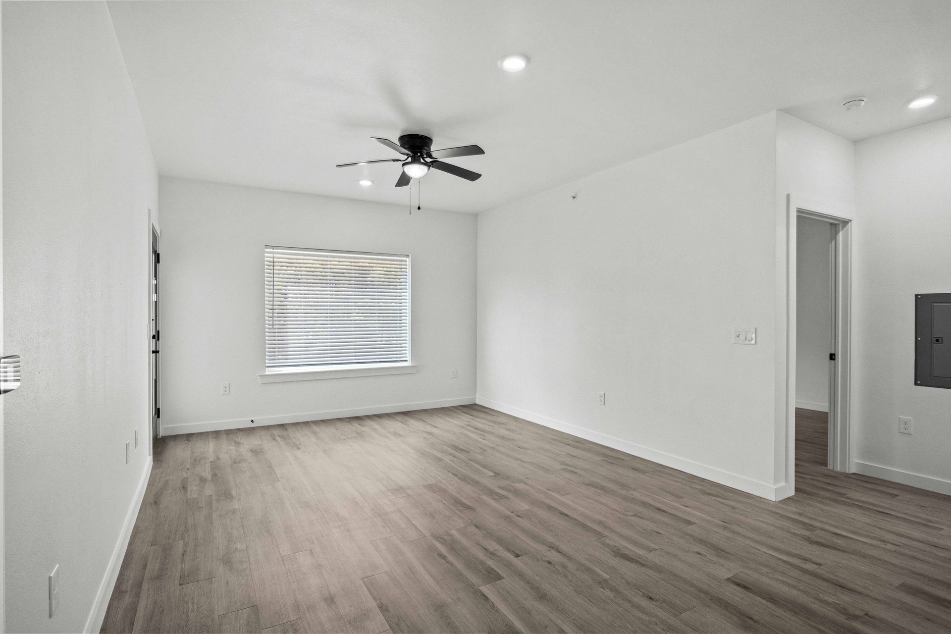 Empty room with light wood flooring, white walls, window, ceiling fan, and open doorway.