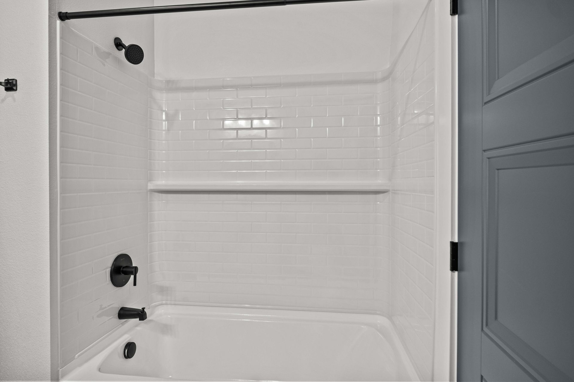 White bathroom with shower, black fixtures, and white subway tile backsplash.