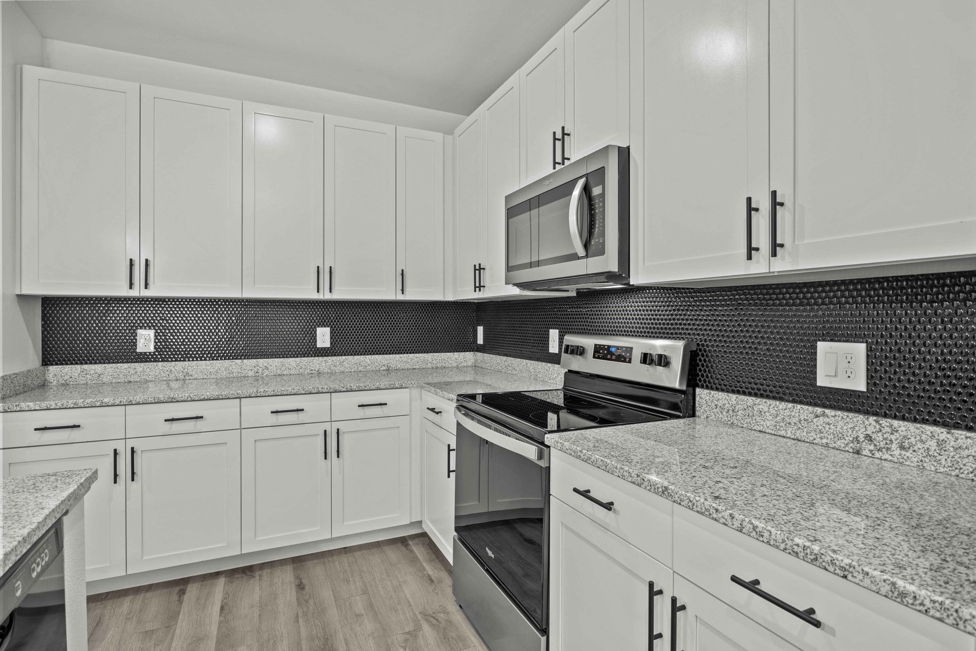 White kitchen with stainless steel appliances, black backsplash, and gray countertops.