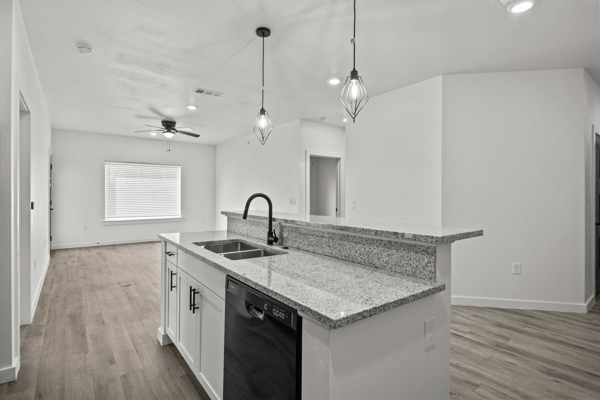 Open-concept kitchen with island, granite countertop, white cabinets, and modern pendant lights.