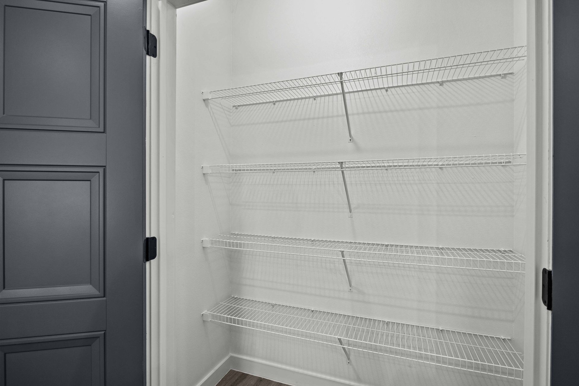 Empty pantry with wire shelving, door on the left, white walls.