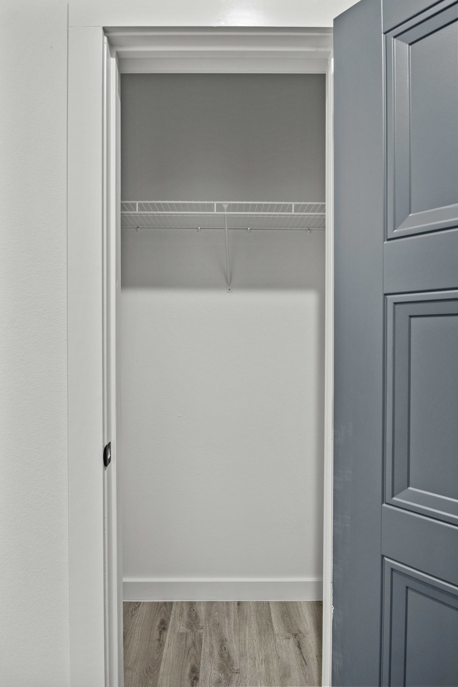 Open closet with white walls, wire shelf, and gray door.