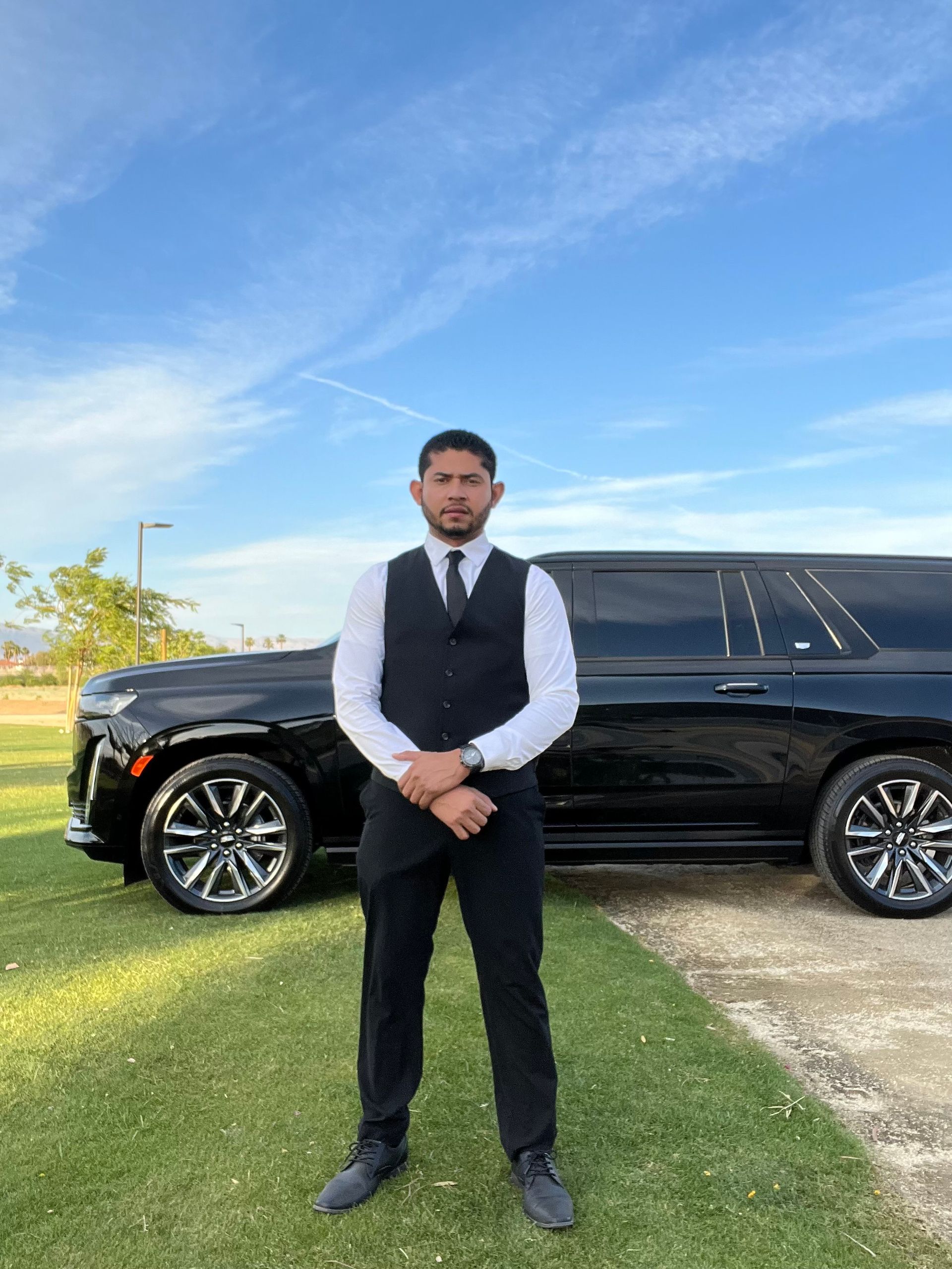 A man in a suit and tie is standing in front of a black limousine.