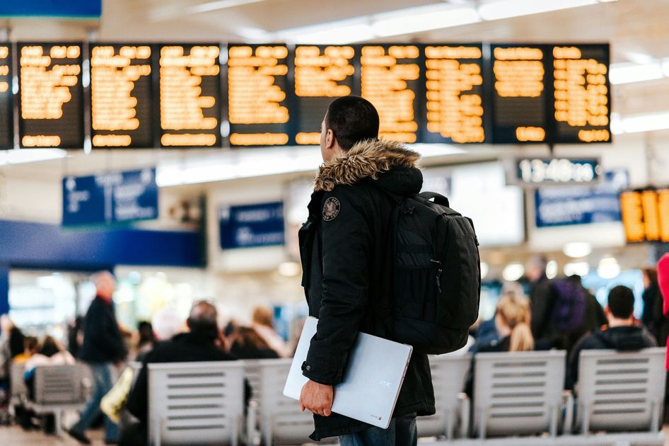 A man is holding a laptop in an airport waiting area.