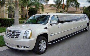 A white limousine is parked on the side of the road in front of a house.