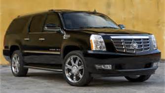 A black cadillac escalade is parked in front of a yellow wall.