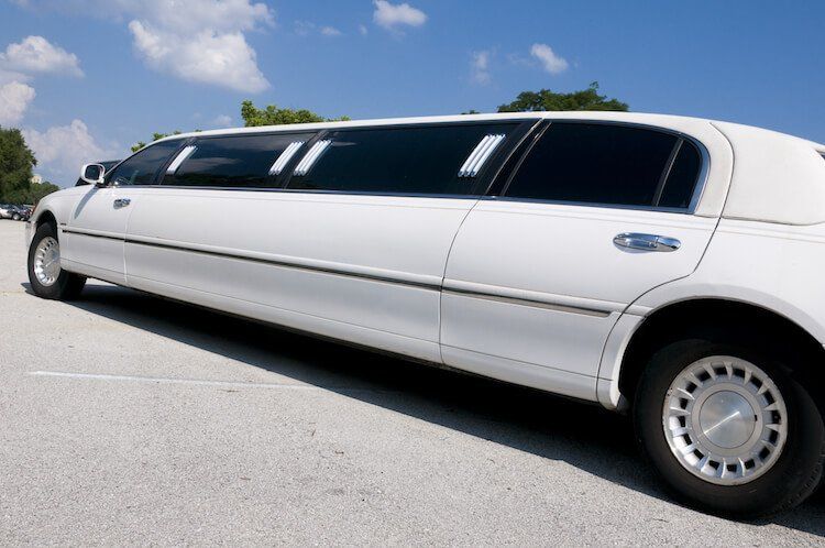 A white limousine is parked in a parking lot on a sunny day.