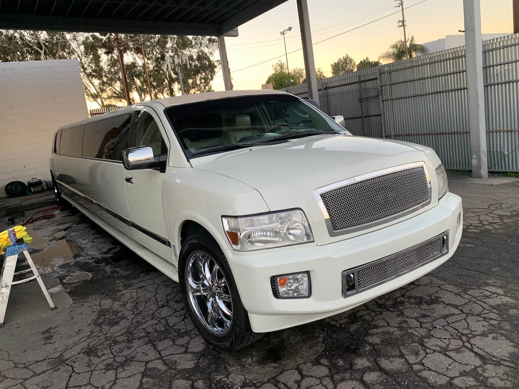 A white limousine is parked under a canopy in a parking lot.