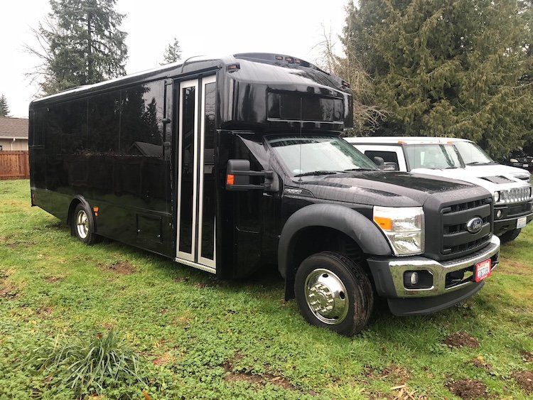 A black bus is parked next to a white truck in a grassy field.
