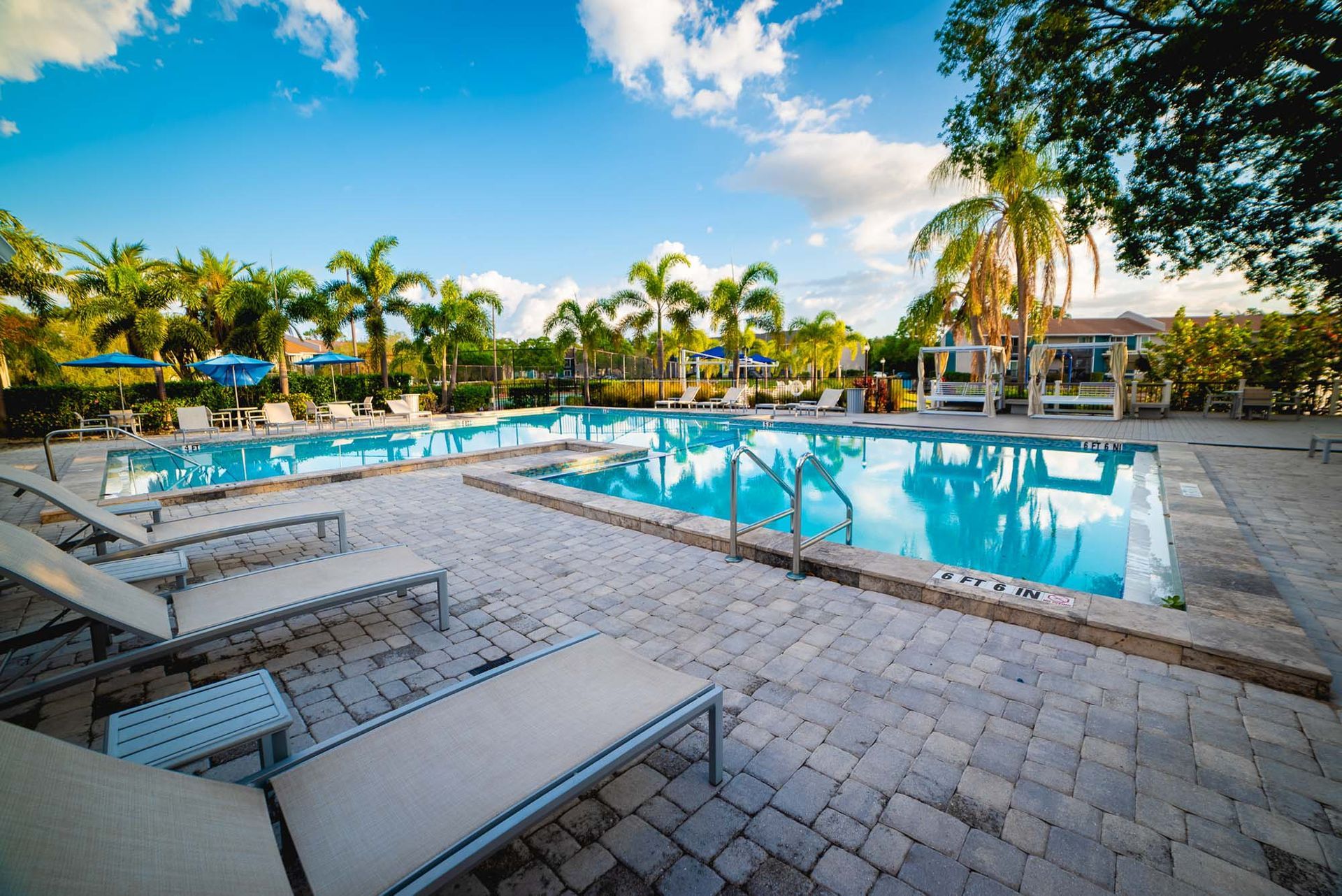 A large swimming pool surrounded by chairs and palm trees on a sunny day at Trellis at The Lakes.