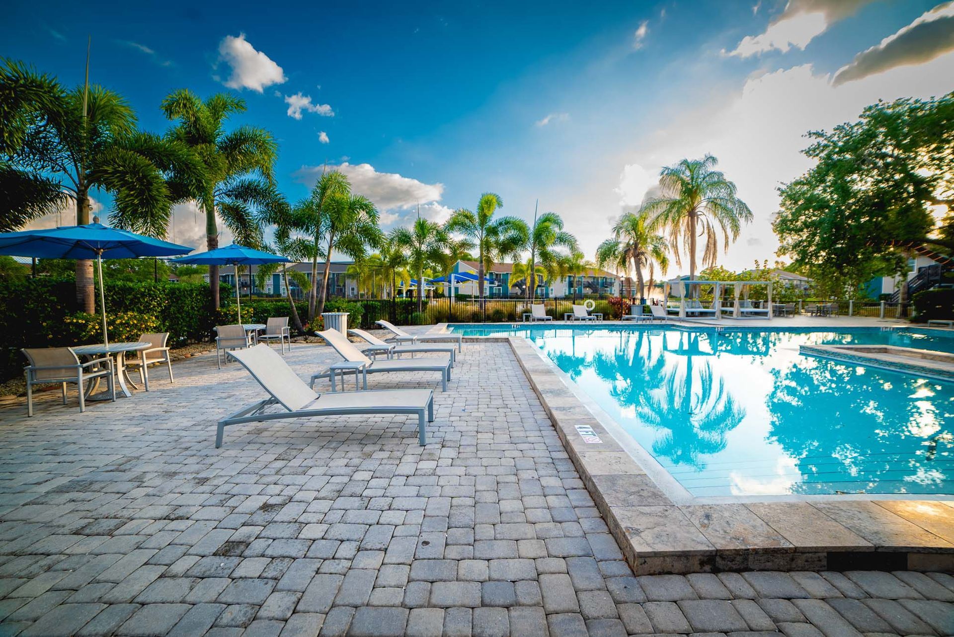 Luxury Apartments for Rent in St. Petersburg - Trellis at the Lakes - Pool with Tables, Umbrellas, Lounge Chairs, and Palm Trees.