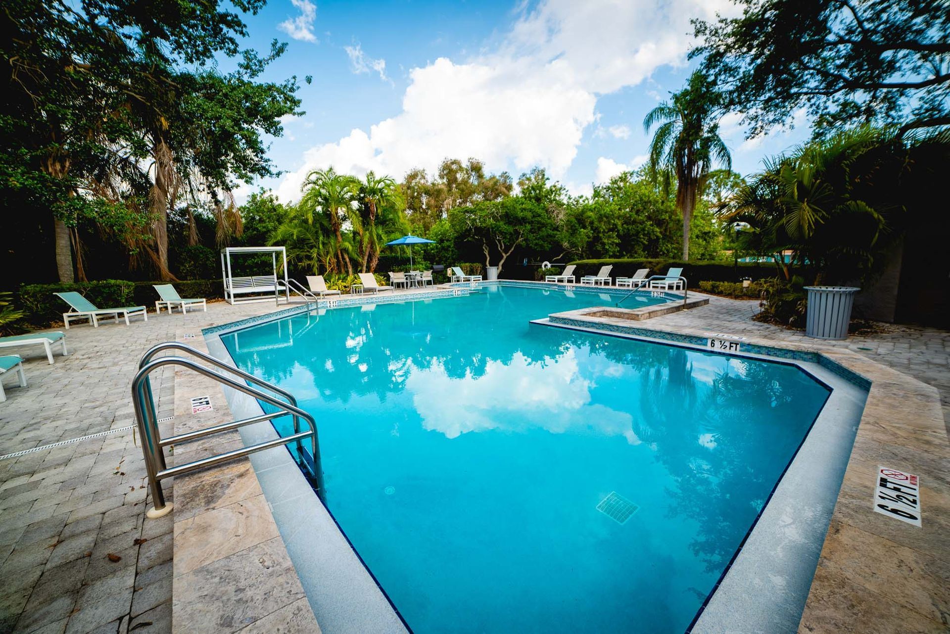 Luxury Apartments for Rent in St. Petersburg - Trellis at the Lakes - Pool with Tables, Umbrellas, Lounge Chairs, and Palm Trees.