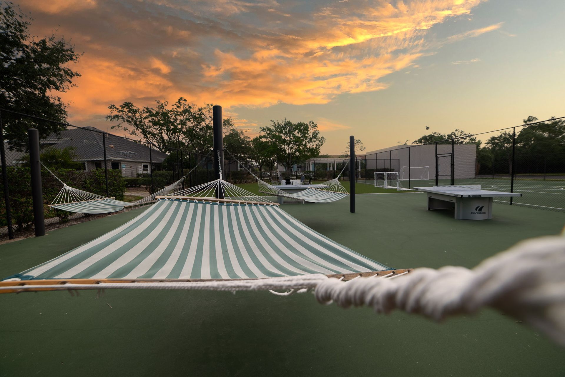 A hammock is hanging from a rope on a tennis court at sunset at Trellis at The Lakes.