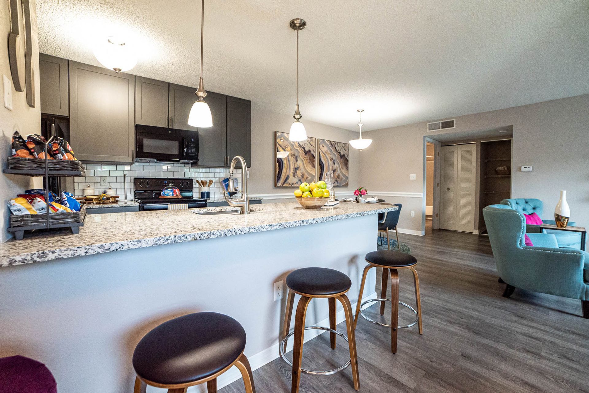 A kitchen with granite counter tops and stools in a living room at Trellis at The Lakes.