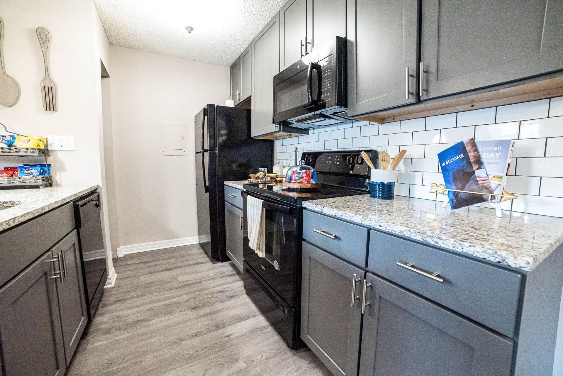 St. Petersburg FL Luxury Apartments - Trellis at the Lakes - Kitchen with Granite-Style Countertops, Grey Cabinets, Wood-Style Flooring, and Black Appliances.