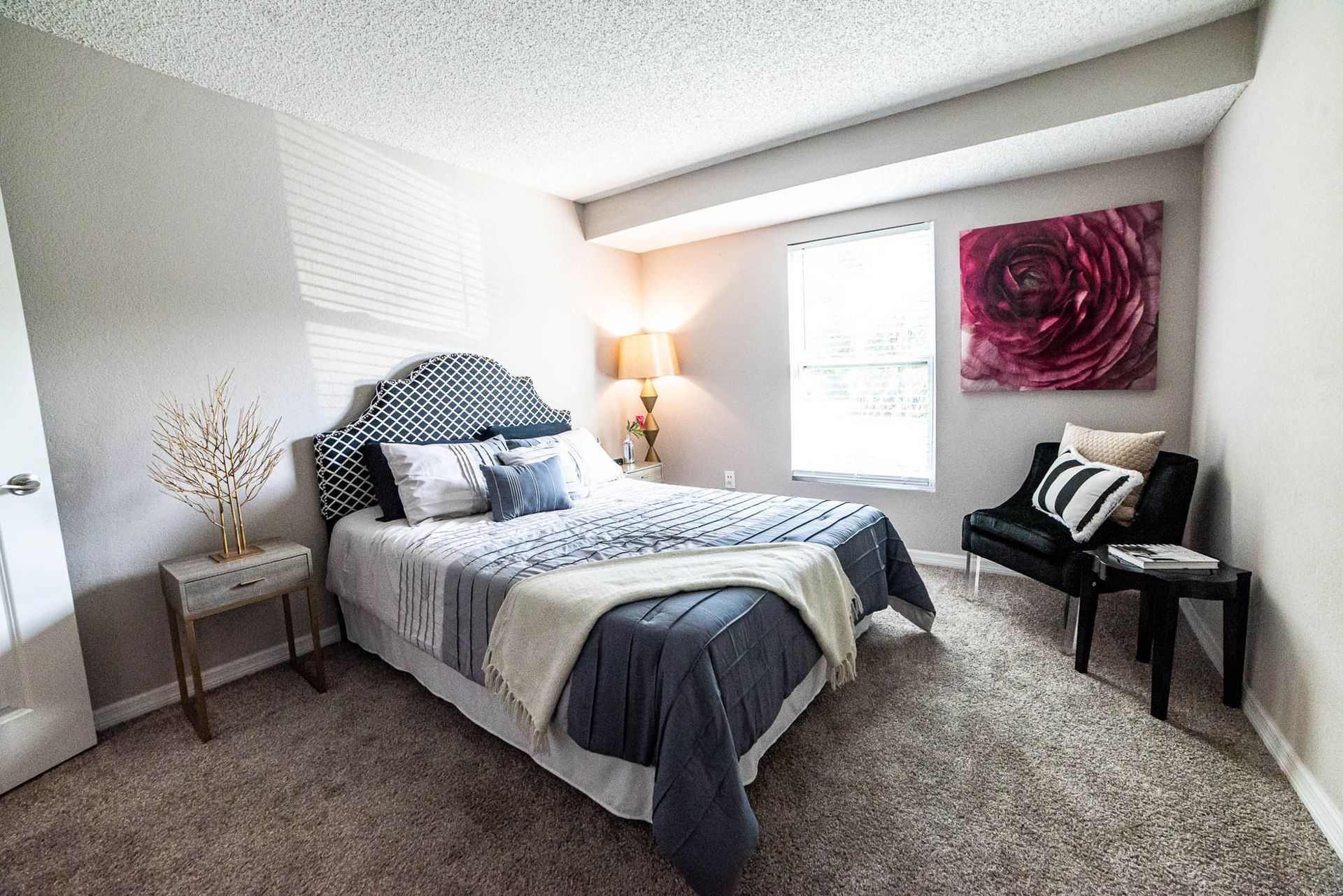 A bedroom with a bed , chair , nightstand and a painting on the wall at Trellis at The Lakes.