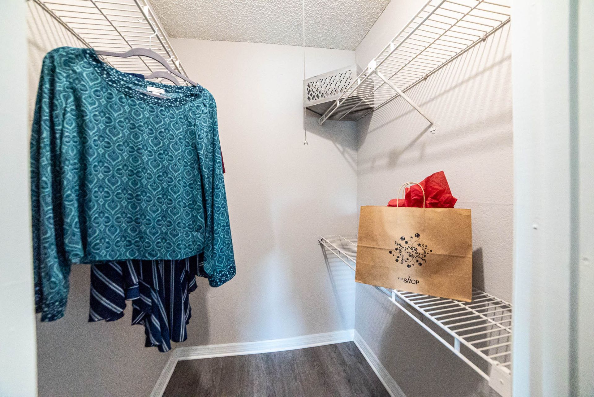 A walk in closet with clothes hanging on racks and shelves at Trellis at The Lakes.