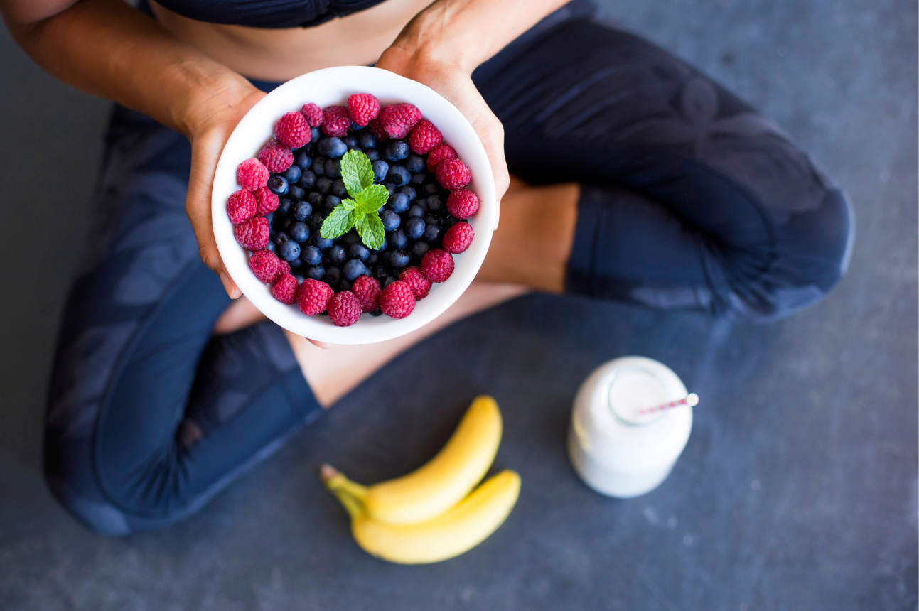 A woman is sitting on the floor holding a bowl of fruit.