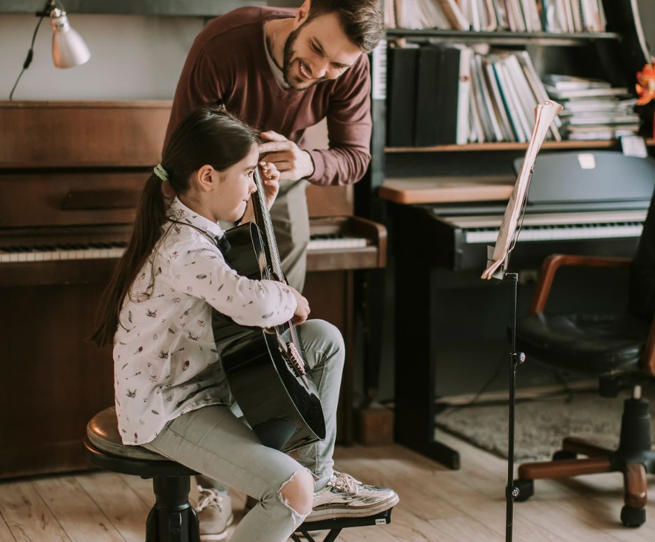 A man is teaching a little girl how to play a guitar.