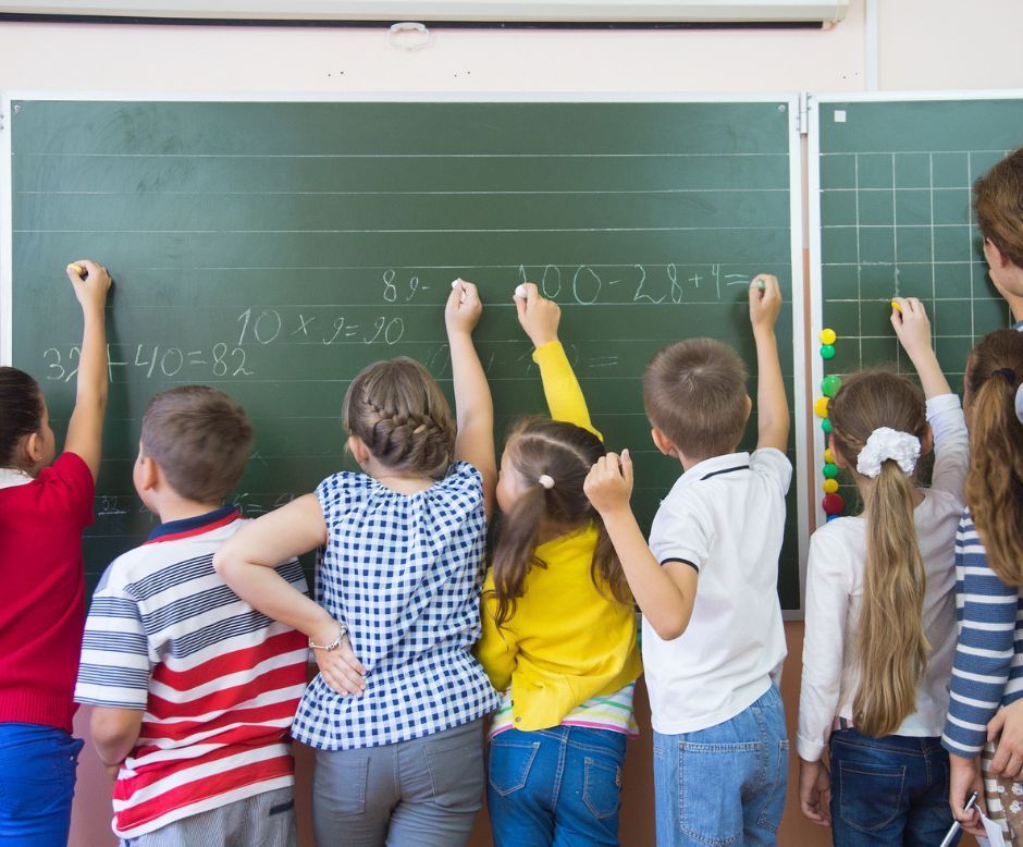 A group of children are writing on a blackboard in a classroom.