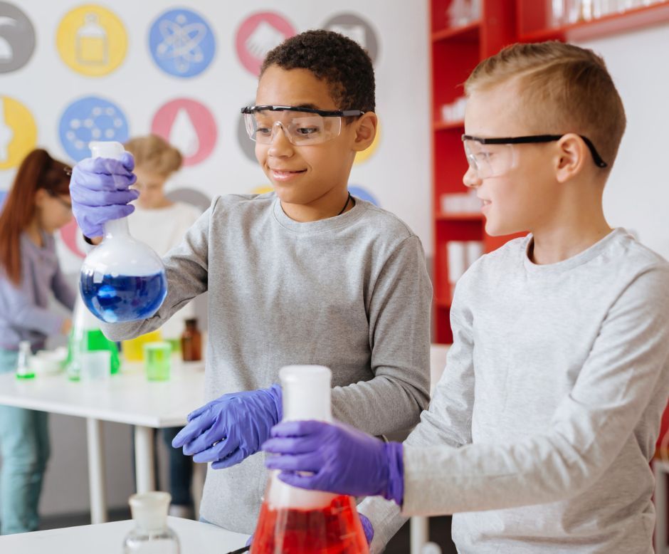 A boy is pouring liquid into a beaker while another boy looks on.