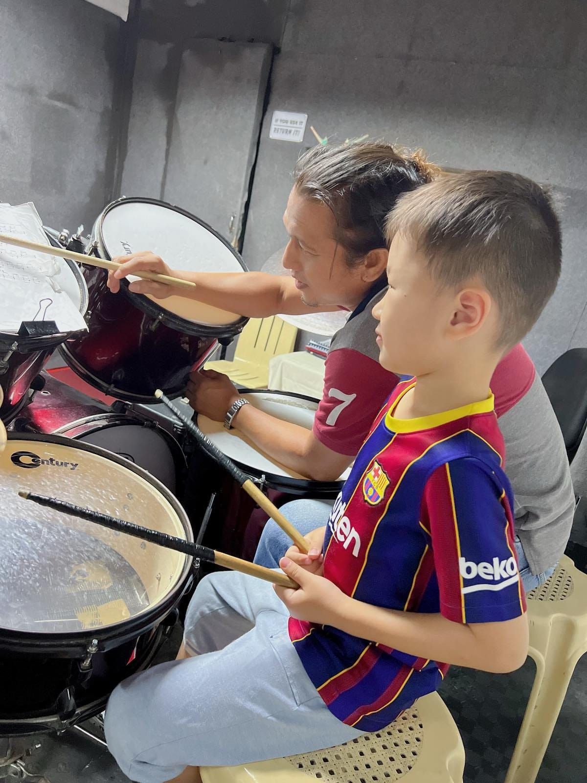 A woman is teaching a young boy how to play drums.