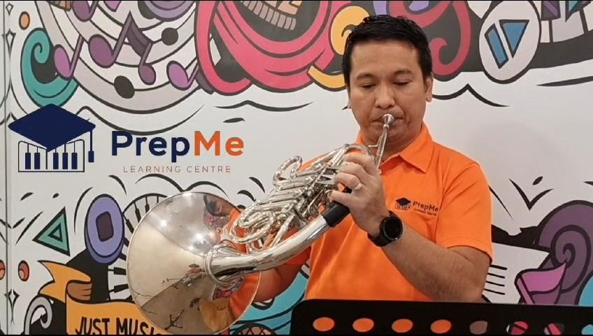 A man in an orange shirt is playing a trumpet in front of a prepme learning center.