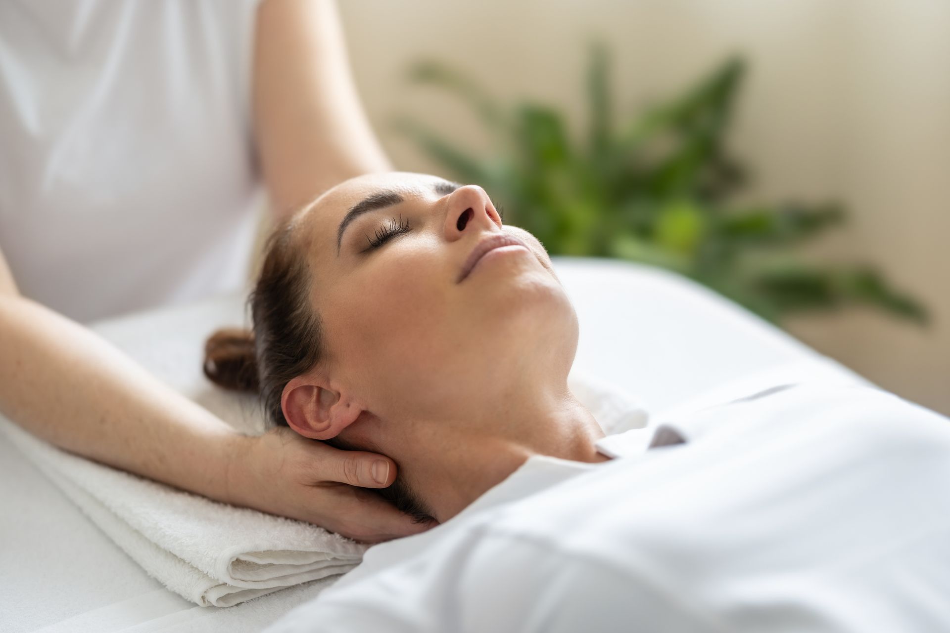 Woman receiving neck massage, lying on a massage table with eyes closed, in a well-lit room. Woman receiving neck massage, lying on a massage table with eyes closed, in a well-lit room.