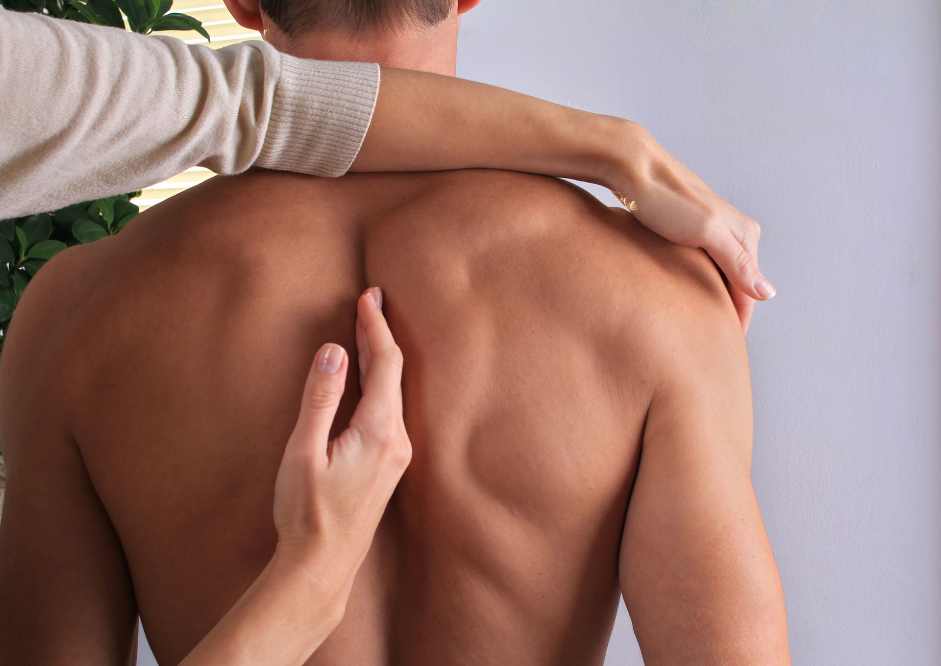 Hands touching a man's bare back; examining his spine.