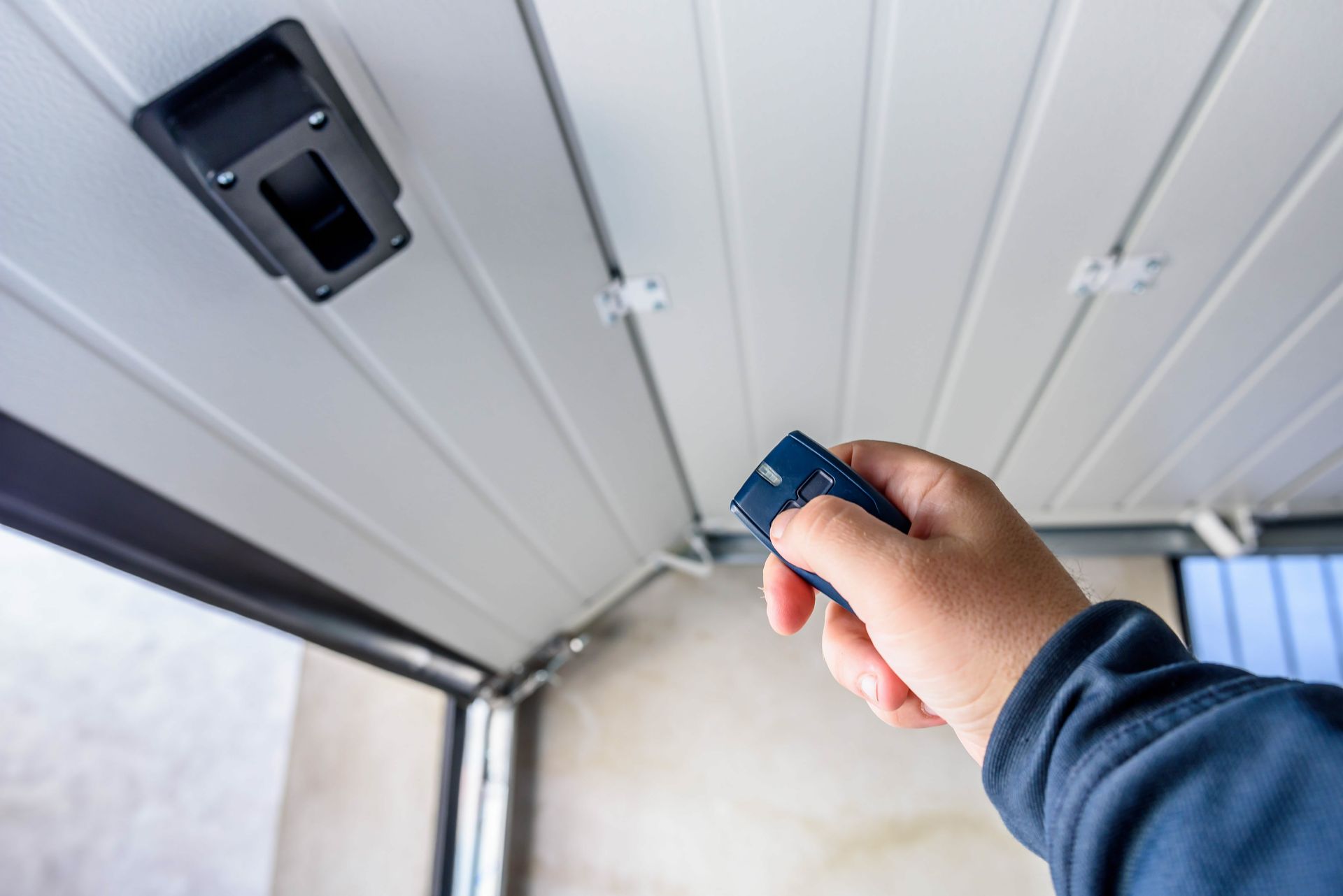 Hand using a remote control to operate an automatic garage door opener.