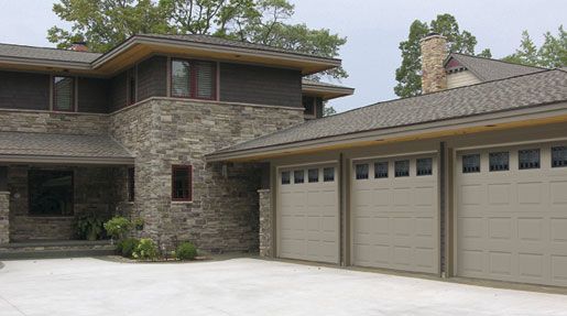 A large house with three garage doors and a driveway in front of it.