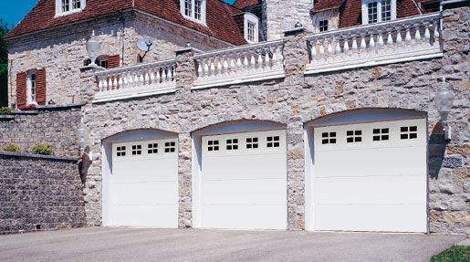 A large stone house with three white garage doors.