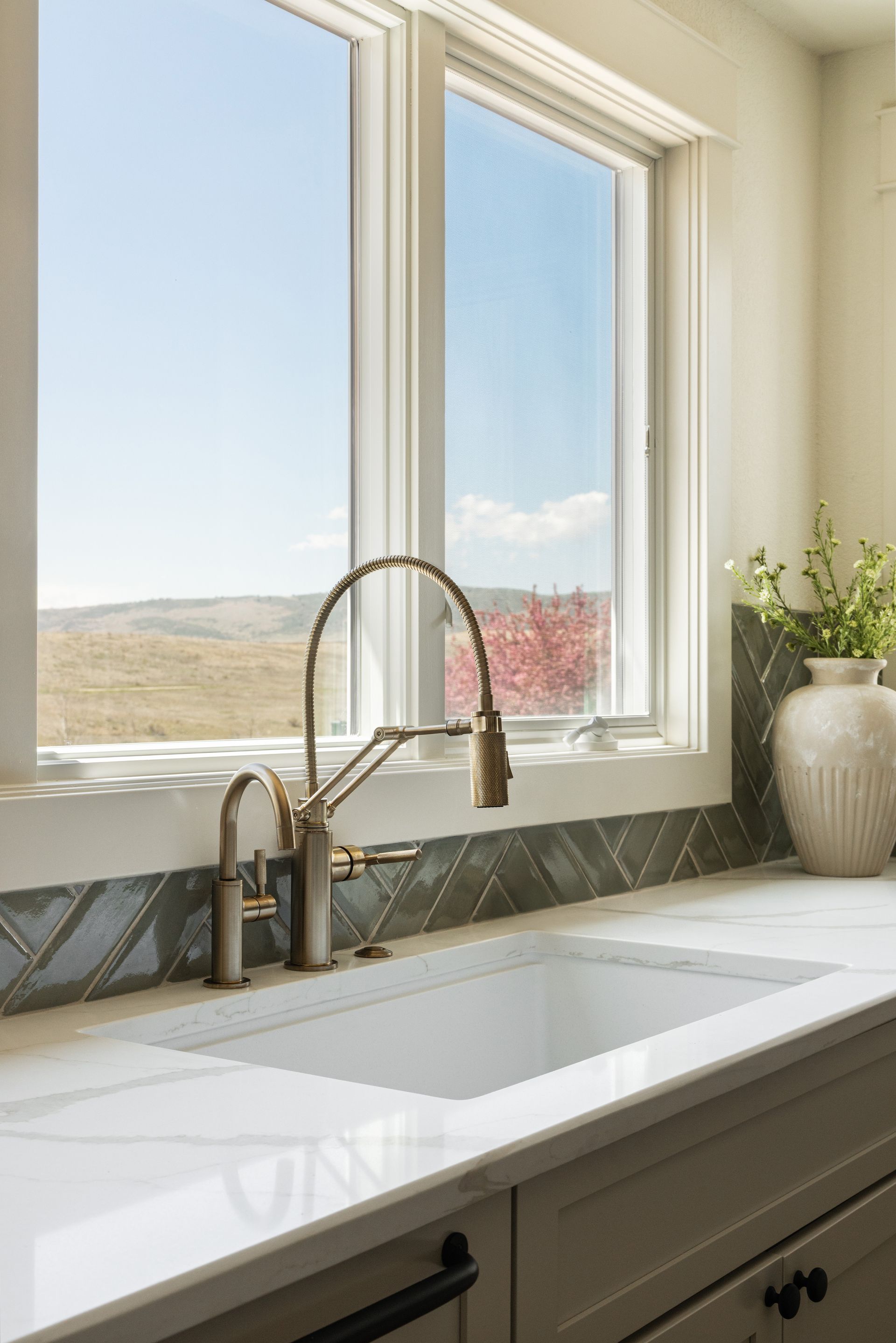 Kitchen sink with brass faucet in front of a window with a view of a sunny landscape.