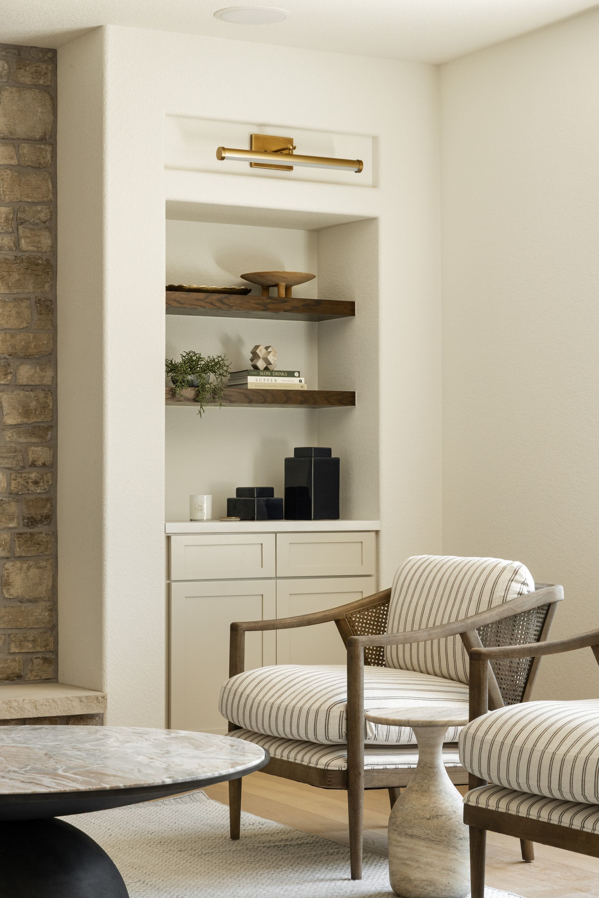 Cozy reading nook with built-in shelves, two patterned armchairs, and a stone accent wall.