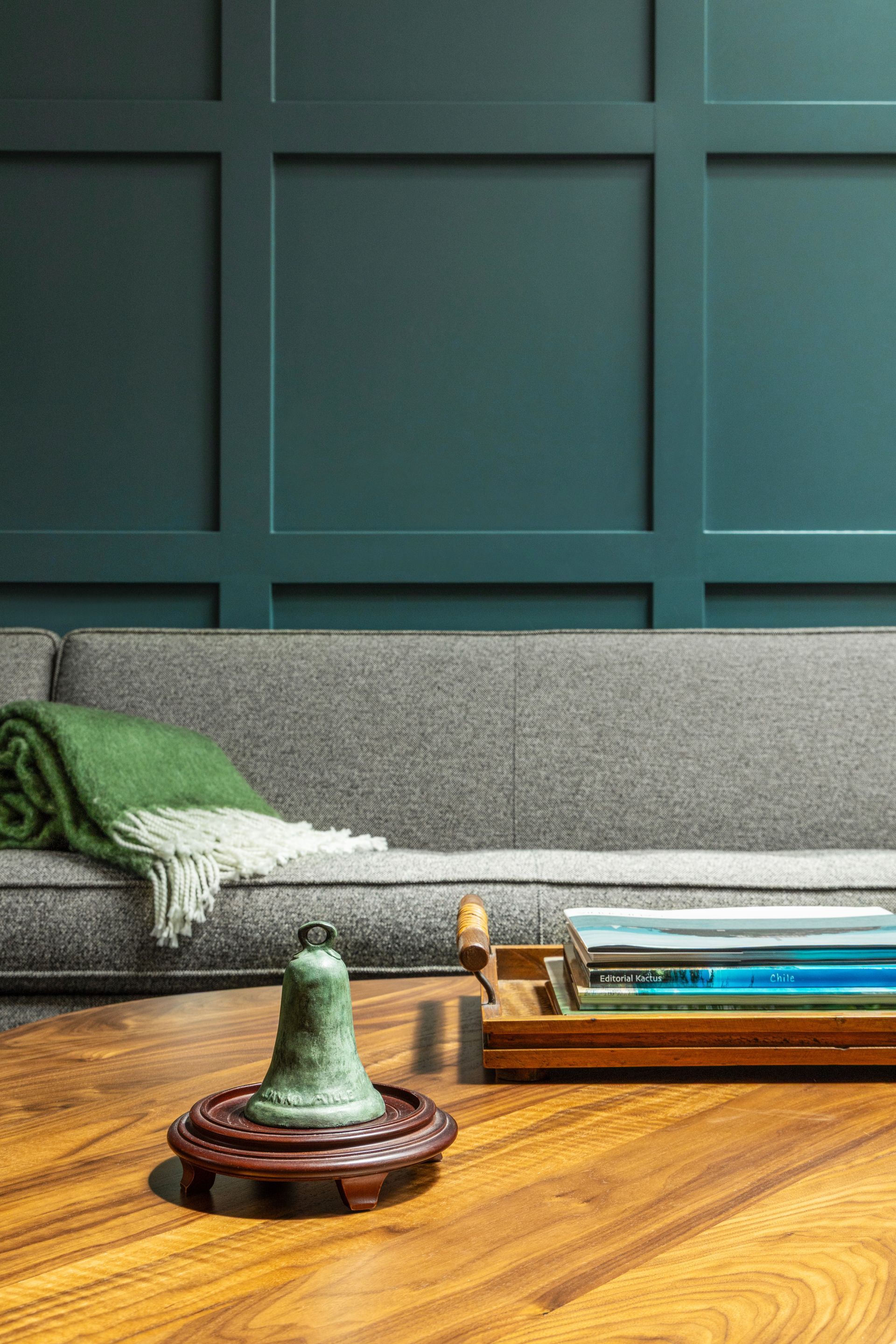 A living room with a teal wall and grey sofa. A green blanket and coffee table with a bell are in the foreground.