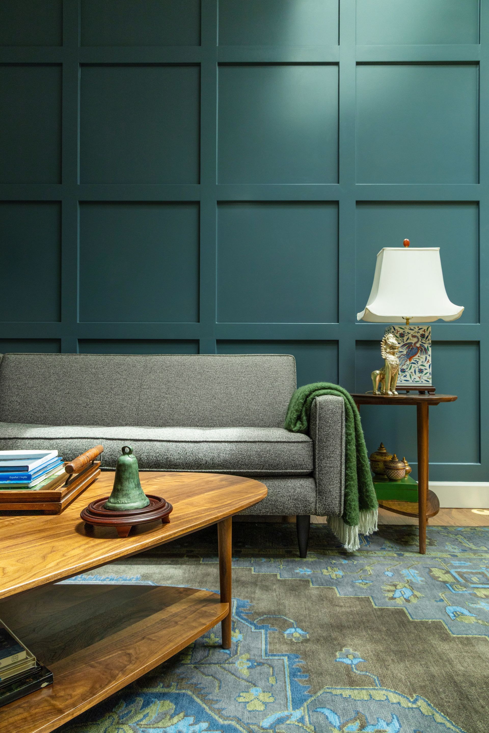 Living room with teal paneled wall, grey sofa, wooden table, and patterned rug.