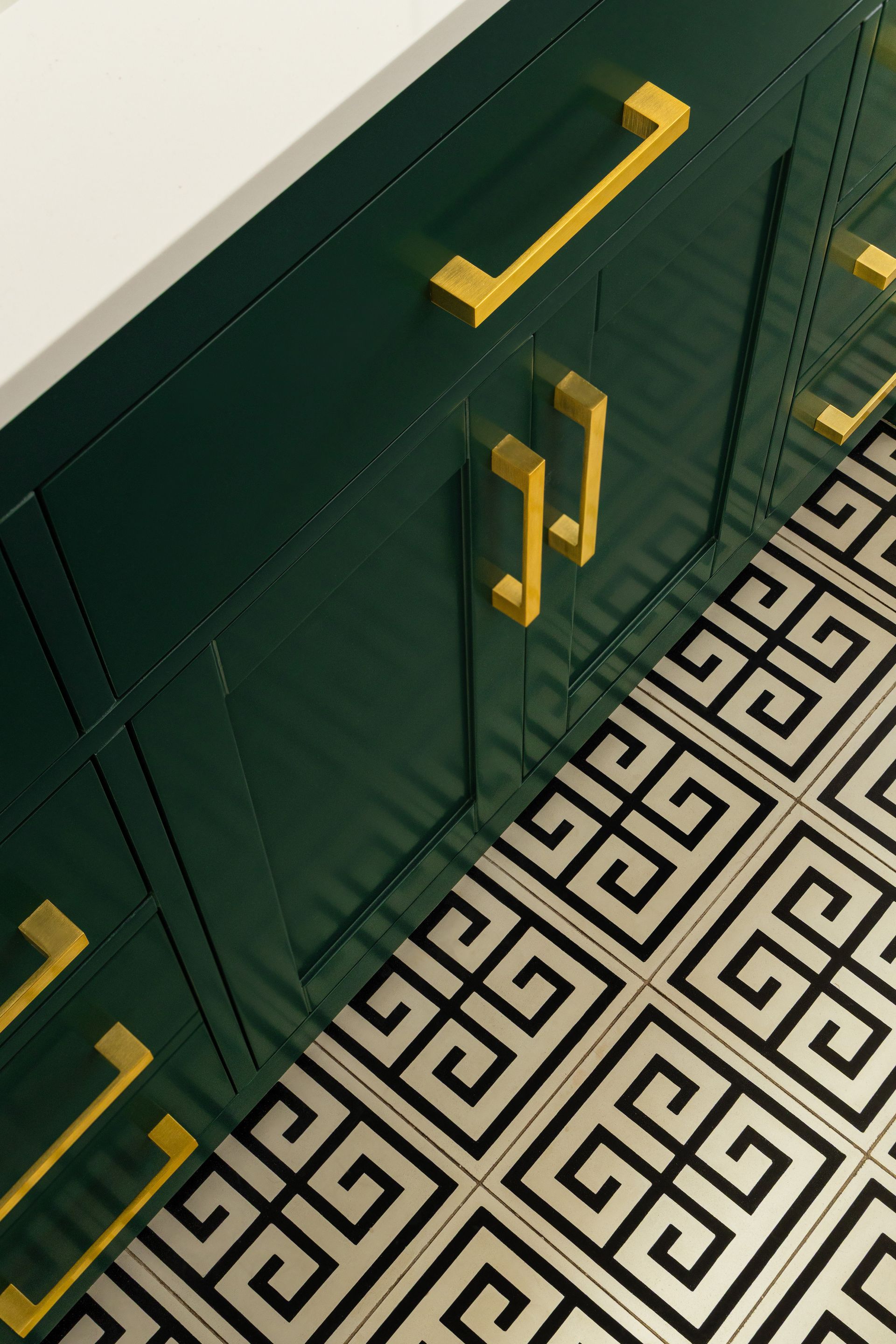 Dark green cabinets with gold handles, white countertop, and patterned floor.