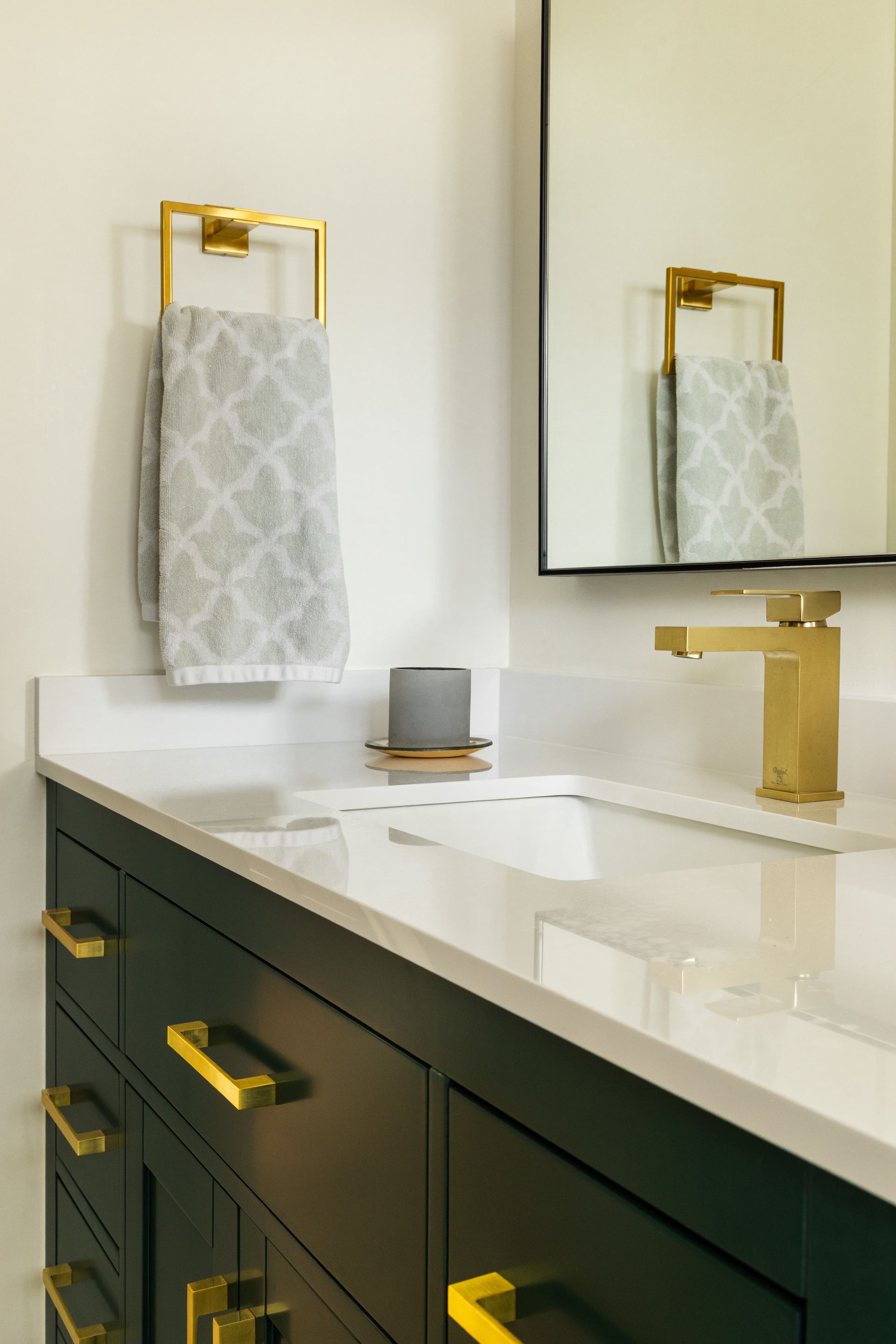 Bathroom with gold fixtures, black vanity, white countertop, gray towel hanging on a gold towel ring.