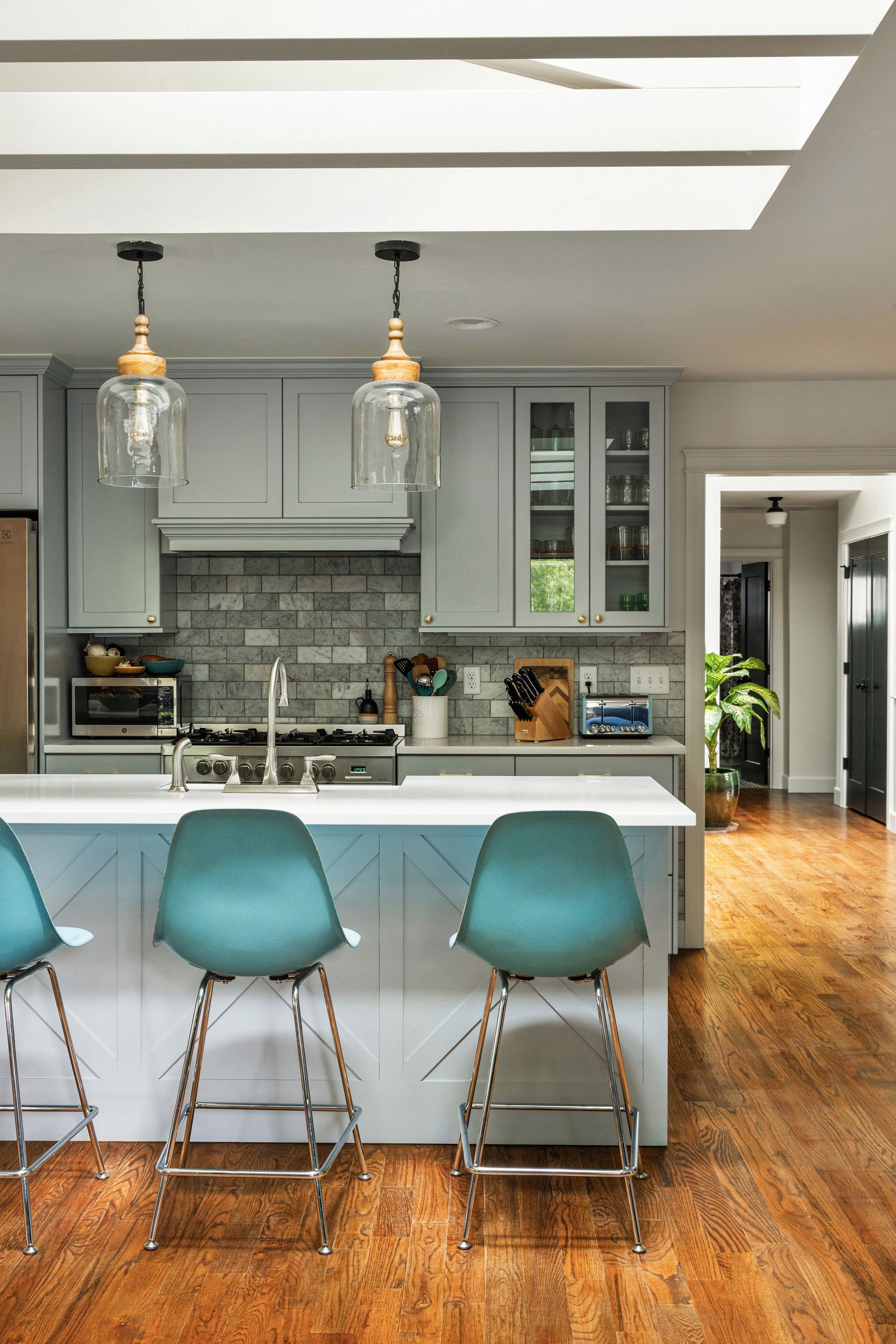 Modern kitchen with teal barstools at a white island, grey cabinets, and pendant lights.