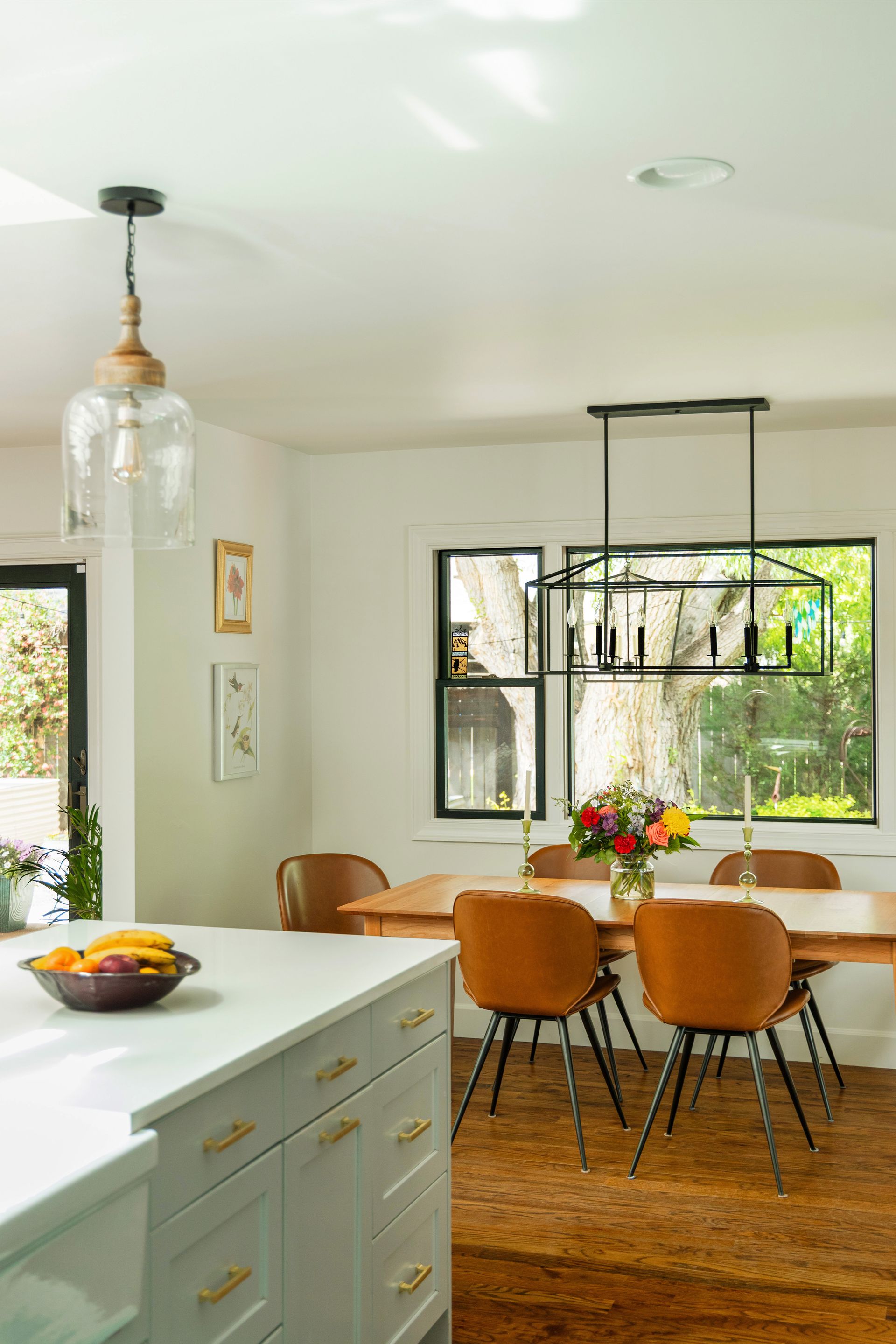 Kitchen with white countertops, dining table with brown chairs, and a floral centerpiece.