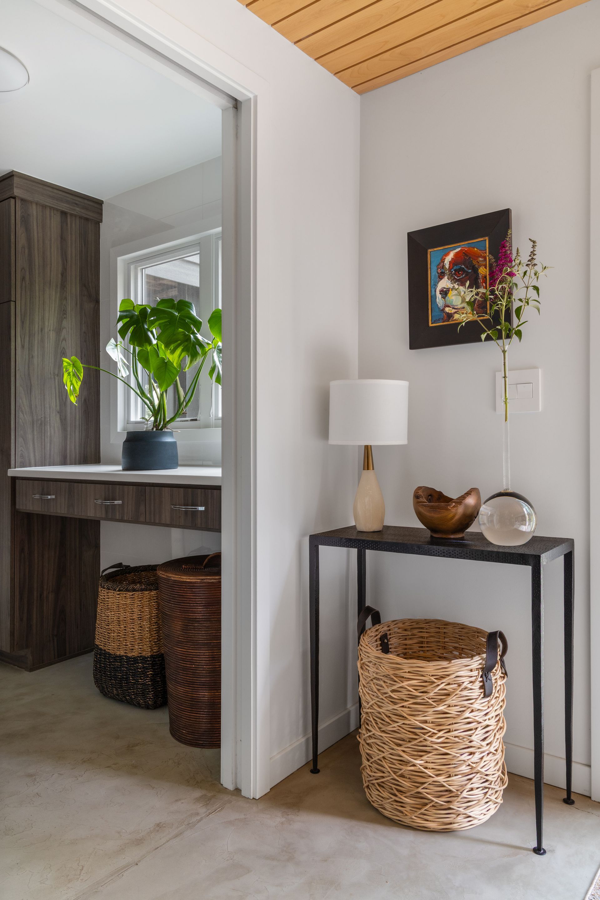 Entryway with a console table, baskets, and built-in workspace visible through a doorway. Neutral tones.