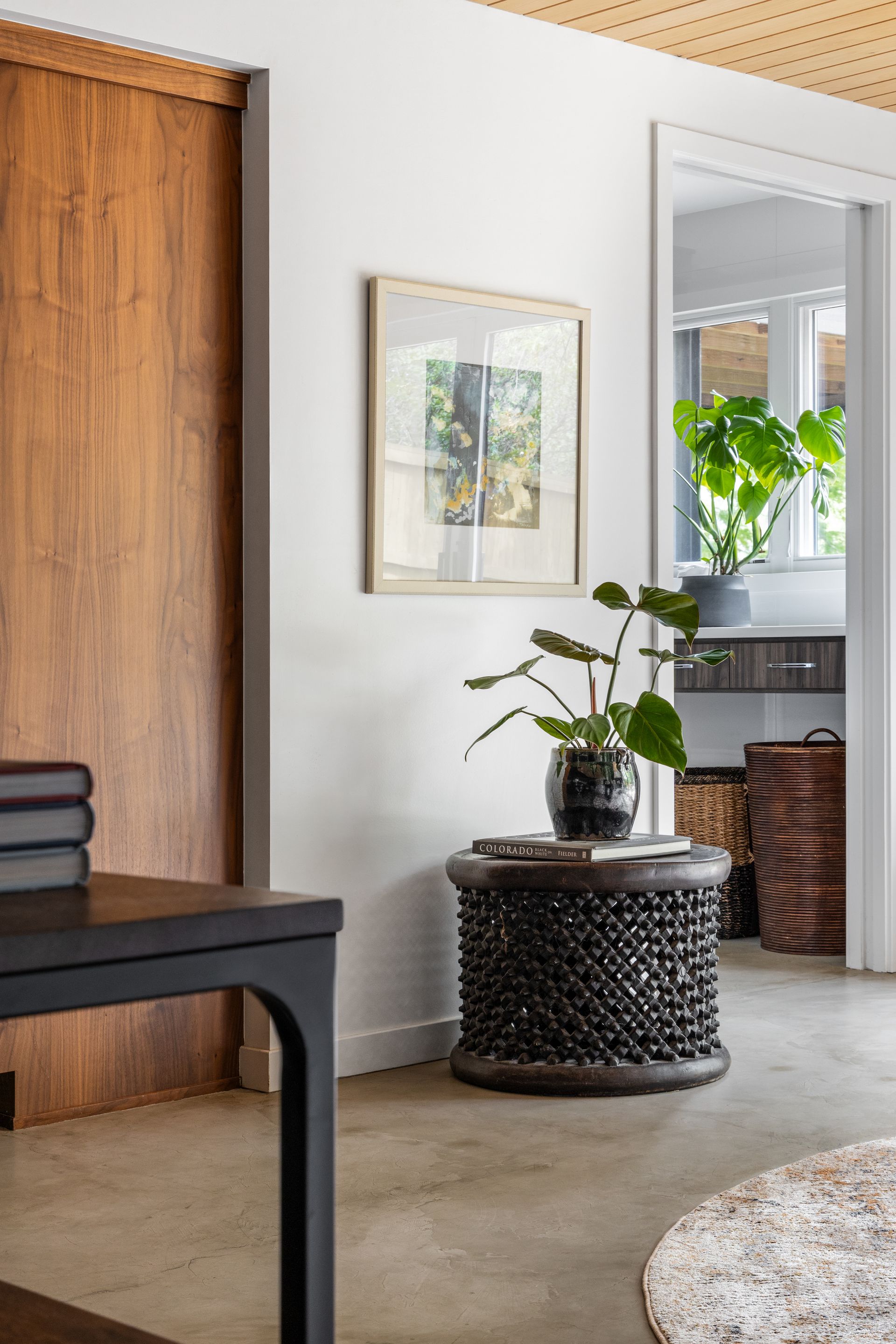 Interior scene: a wooden desk and a black beaded side table next to a white wall with artwork and a door.