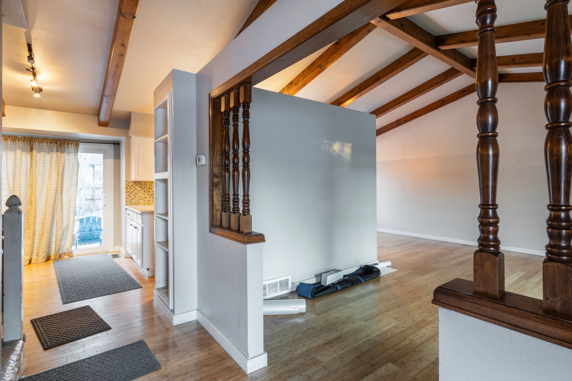 Interior view of a home with wooden beams, hardwood floors, and a partial wall with vertical slats.