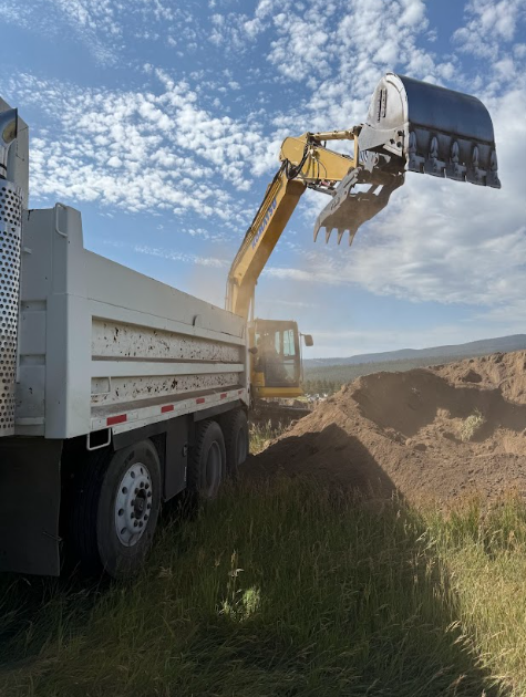 Mini-excavator digging near a house under construction; piles of dirt and a septic tank visible.