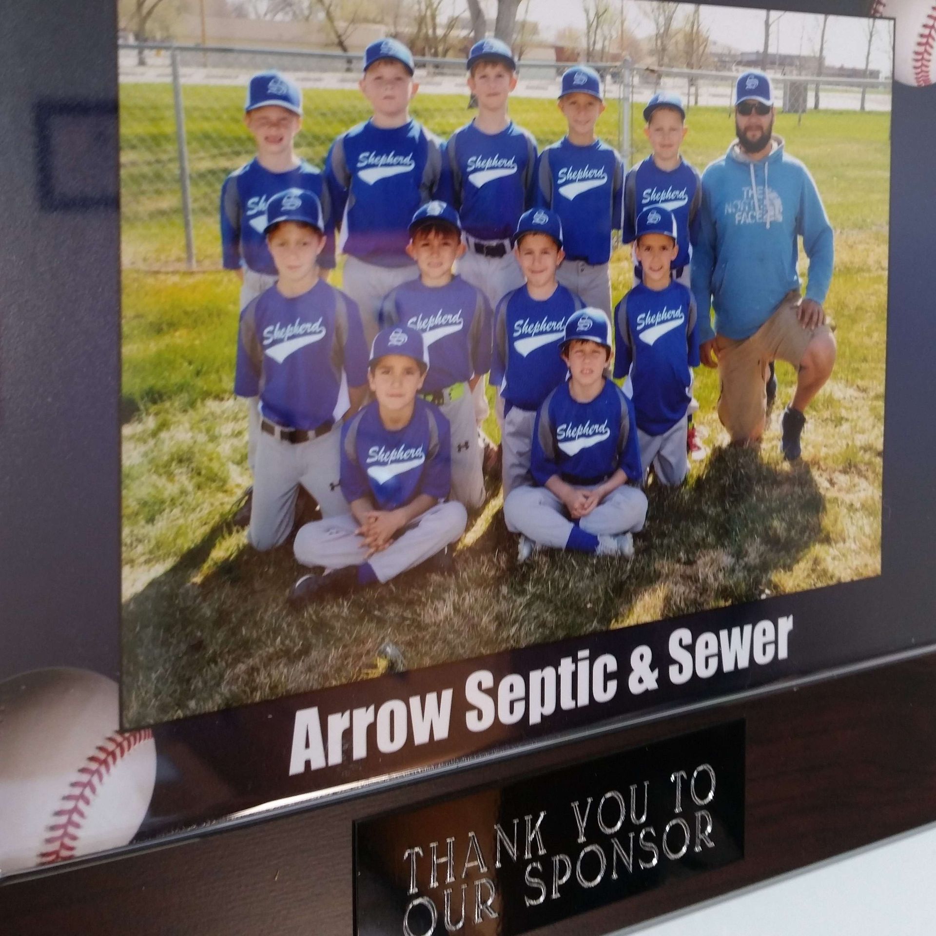 Youth baseball team in blue jerseys, sponsored by Arrow Septic & Sewer, posing on a field.
